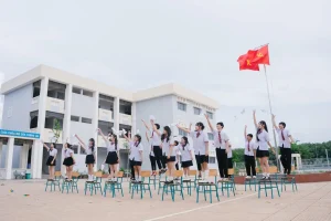 Nhóm học sinh đứng trên ghế trong sân trường dưới cờ đỏ