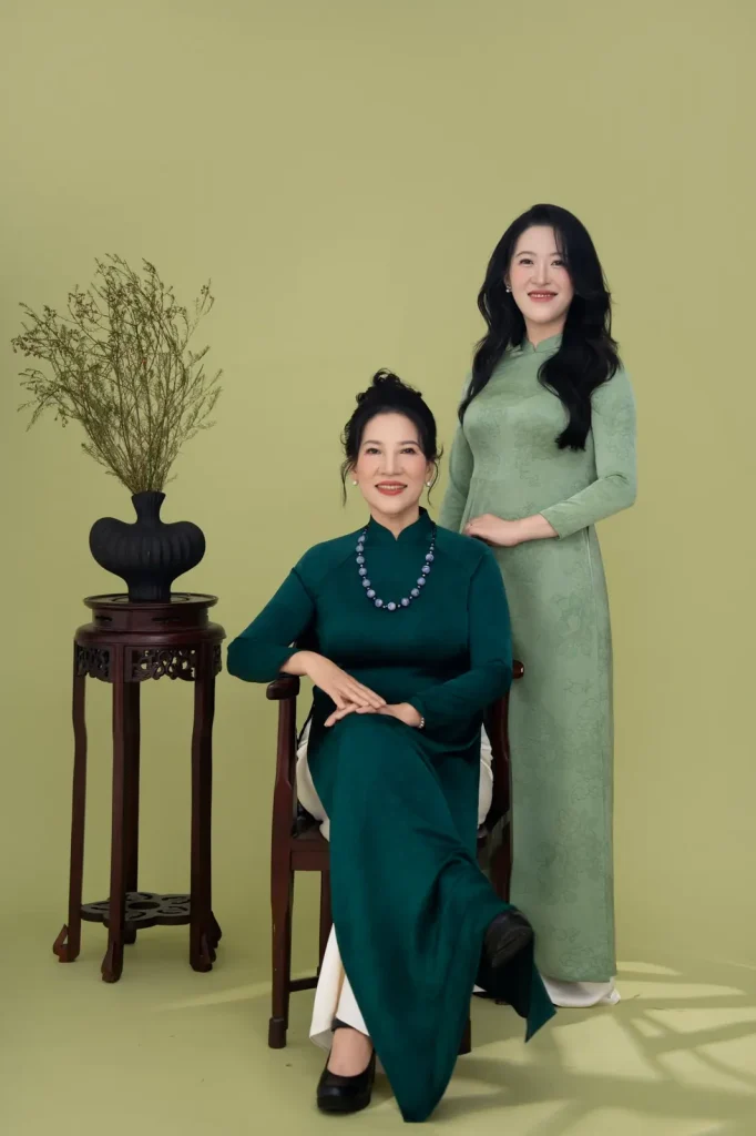 Bà ngồi trên ghế gỗ, cười nhẹ nhàng khi chụp ảnh cùng gia đình