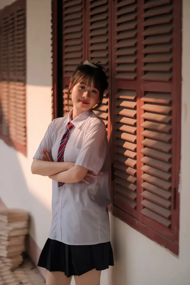 Nữ sinh mặc đồng phục đứng bên cửa chớp gỗ có nắng