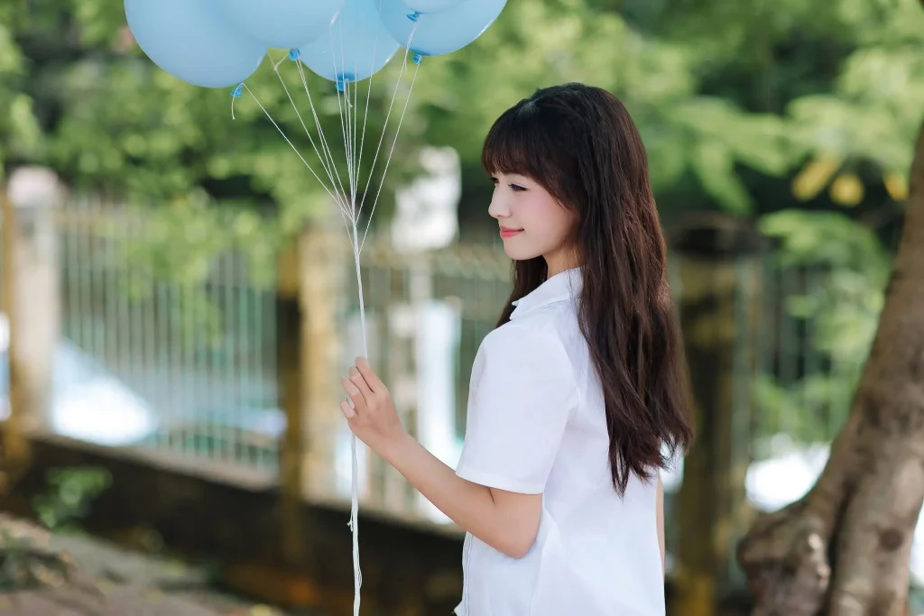 Bạn nữ mặc đồng phục cầm chùm bóng xanh ngoài trời
