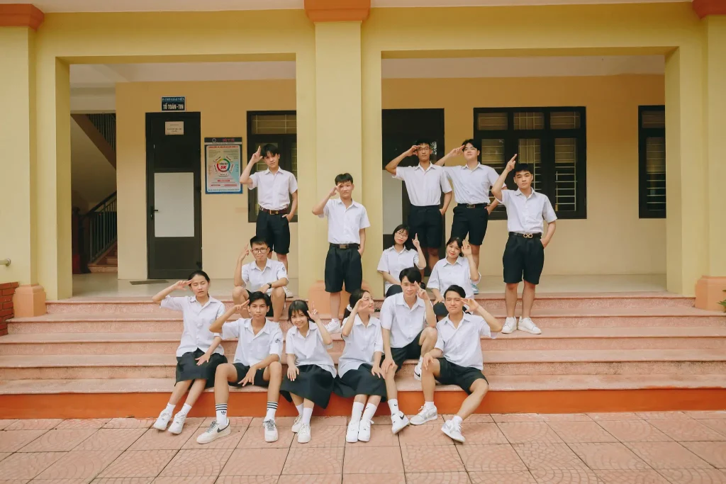 Nửa ngày để có một thời cùng nhau – Lịch chụp kỷ yếu 1 Tập thể học sinh mặc sơ mi trắng đứng trên bậc thềm trước dãy nhà vàng