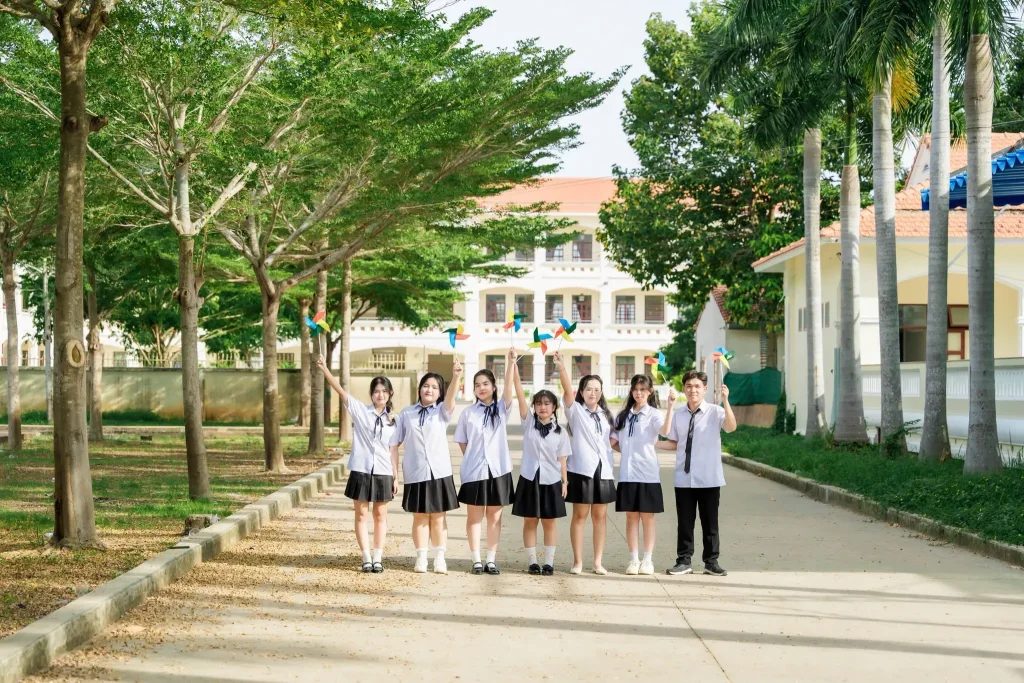 Tập thể học sinh đứng trên lối đi có hàng cây