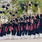Tập thể học sinh mặc áo cử nhân tung mũ trong sân trường