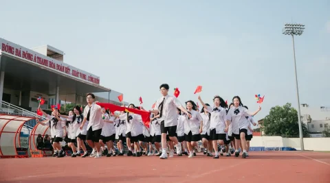 Tập thể học sinh với dải vải đỏ trên sân vận động