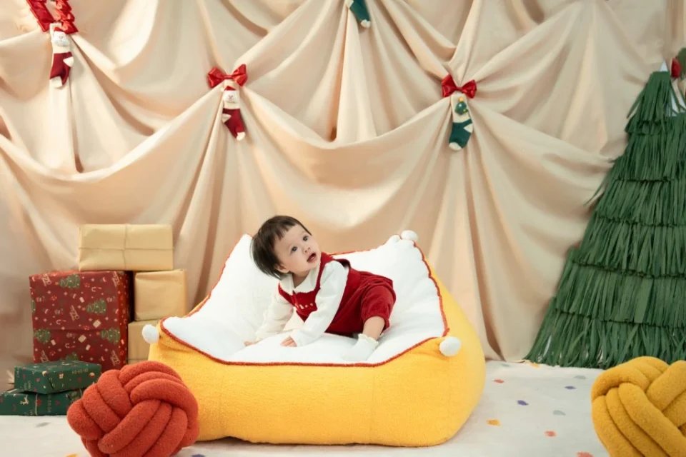 Bé mặc đồ đỏ tựa trên đạo cụ vàng trong bối cảnh Giáng sinh