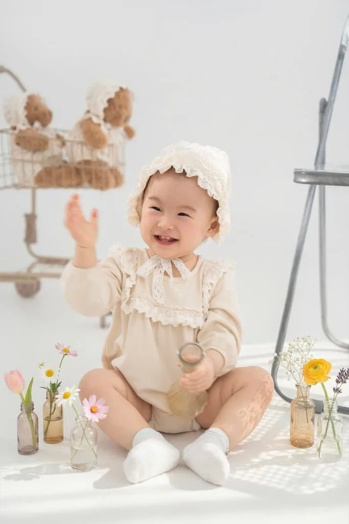 Bé mặc đồ tông be ngồi cùng đồ chơi và phụ kiện trang trí