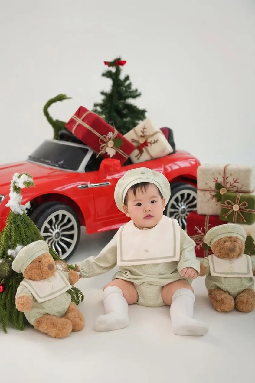 Bé ngồi cạnh ô tô đỏ trong bối cảnh cây thông và quà Noel