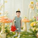 Bé tạo dáng trong bối cảnh cây hoa tông xanh và vàng