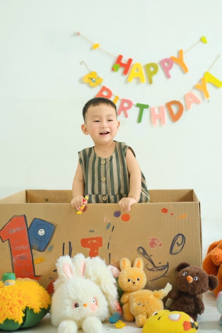 Bé đứng trong hộp quà với các phụ kiện sinh nhật nhiều màu