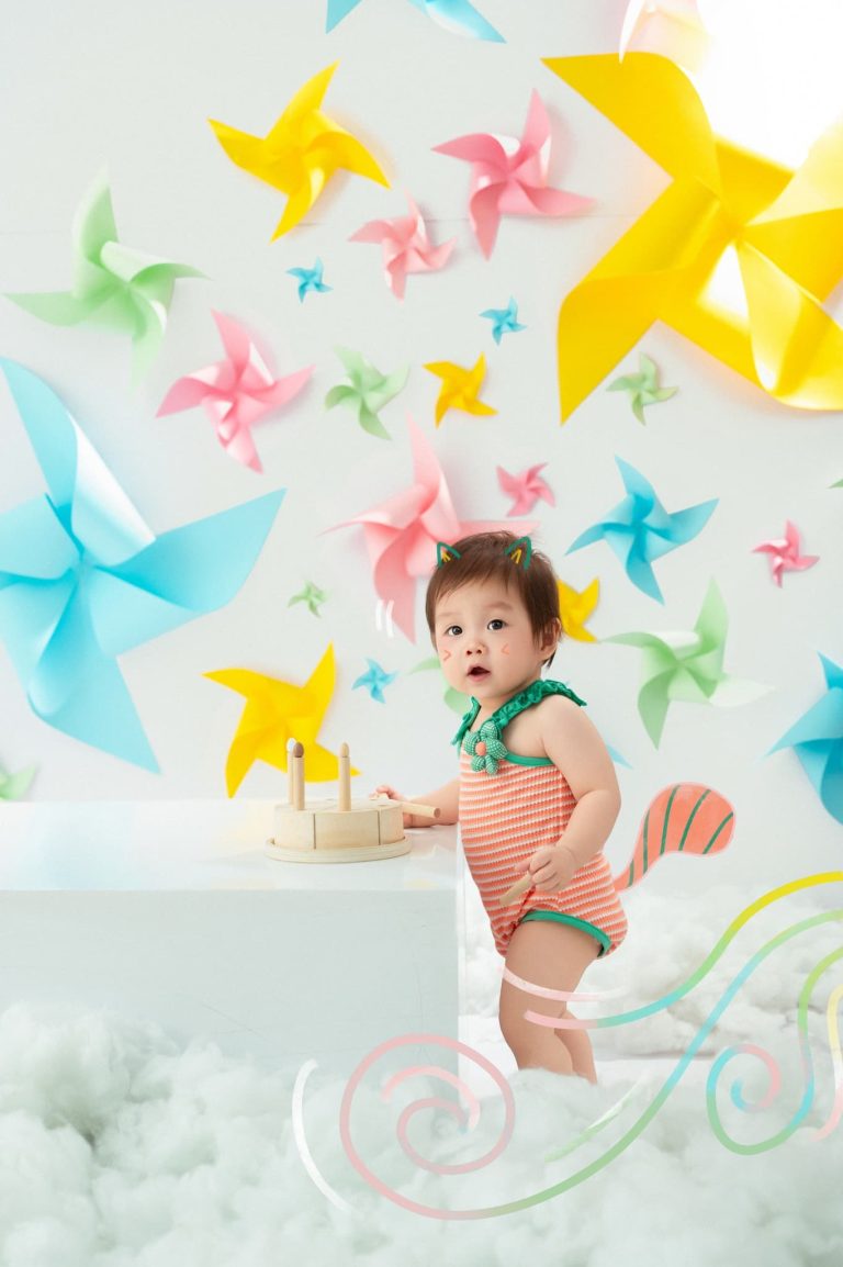 Bé đứng trong bối cảnh giấy màu, chong chóng và cây lá minh họa