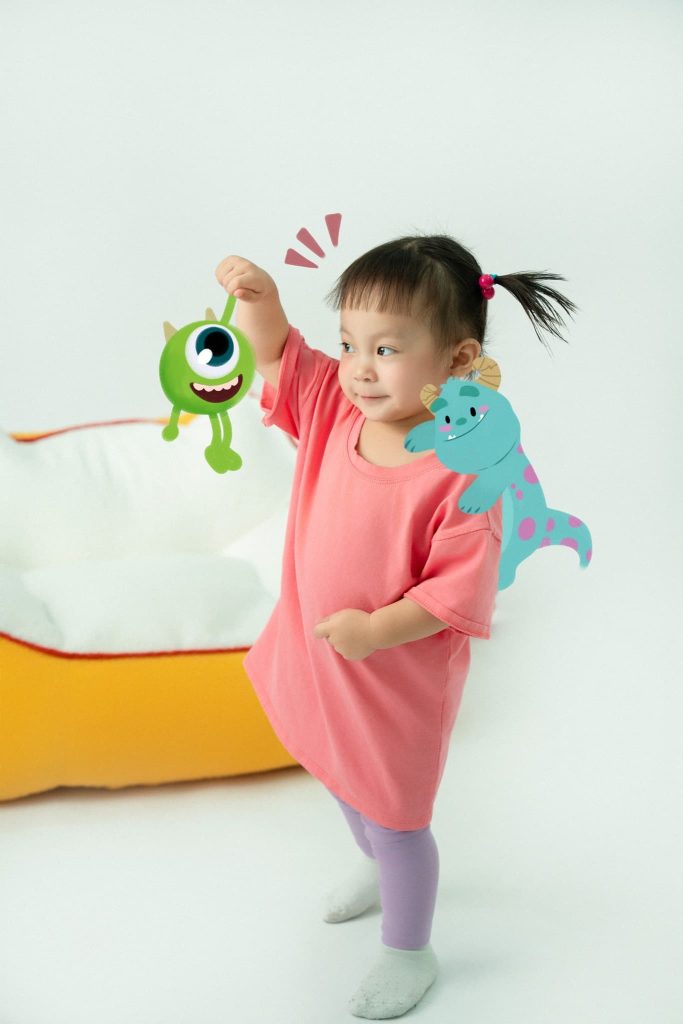Bé mặc đồ hồng đứng cùng các nhân vật hoạt hình minh họa