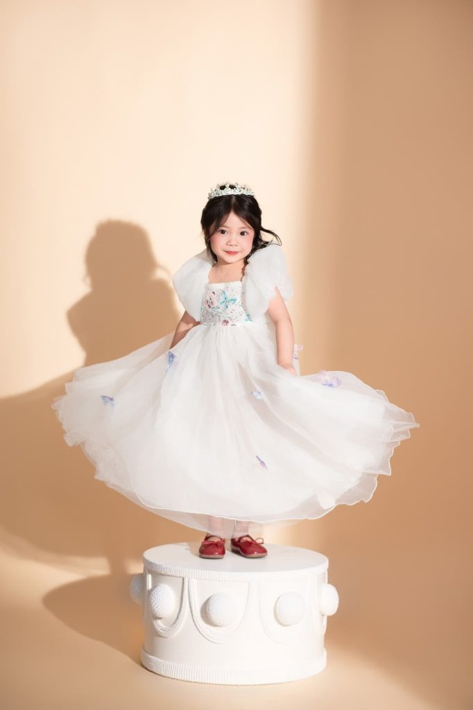 Bé mặc váy sáng màu trong bối cảnh sinh nhật nền kem với bánh trang trí