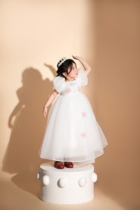 Bé gái mặc váy trắng tạo dáng trên nền màu be