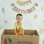 Bé đứng trong hộp quà với phụ kiện sinh nhật trên nền sáng