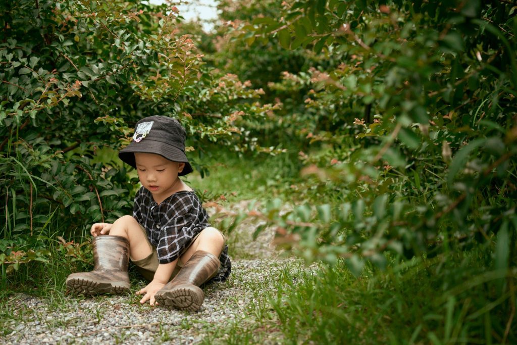 Bé ngồi trên cỏ nhìn đôi ủng của mình