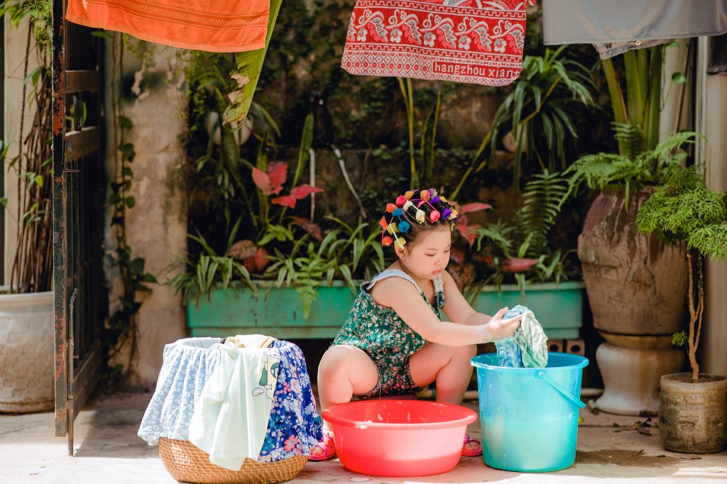 Bé nâng khăn ướt phía trên thùng nước xanh