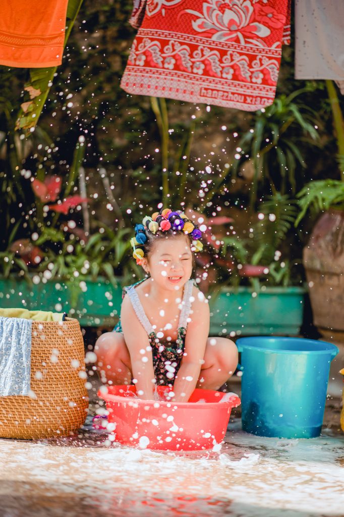 Bé ngồi cạnh chậu đỏ với nước bắn quanh người