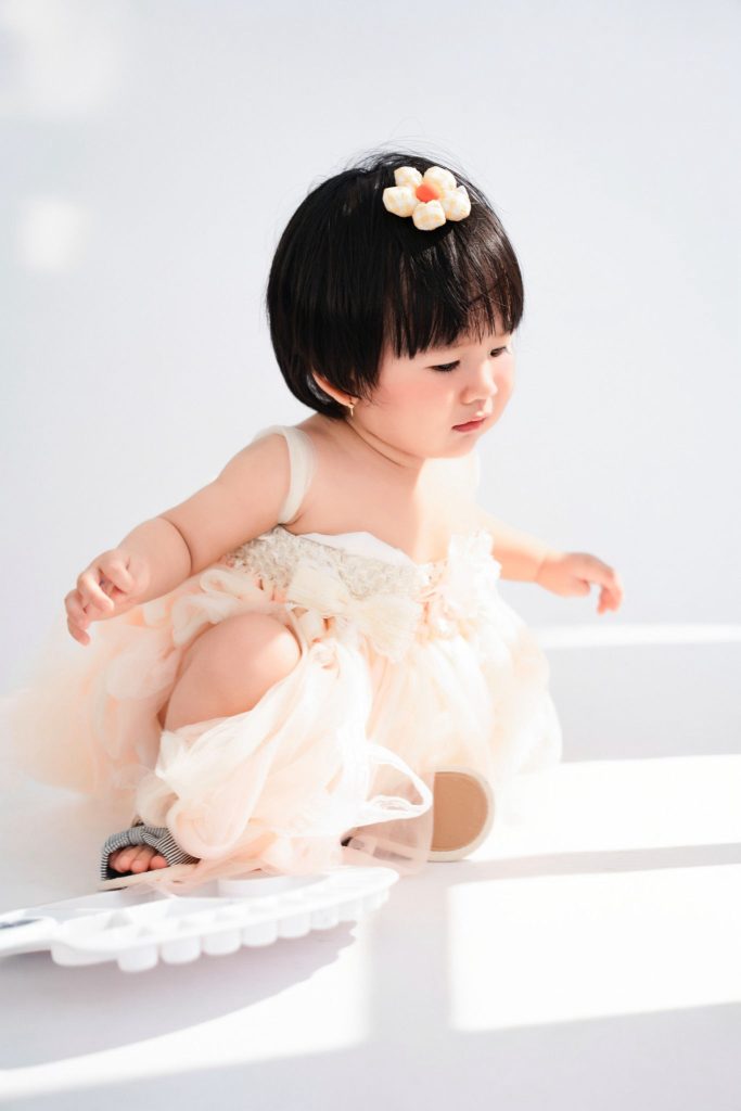 Bé mặc váy trắng ngồi nhìn xuống, hai tay mở rộng