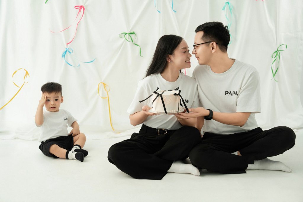 Ba mẹ và bé mặc trang phục trắng, đen, ngồi trên nền sáng trong bộ ảnh gia đình