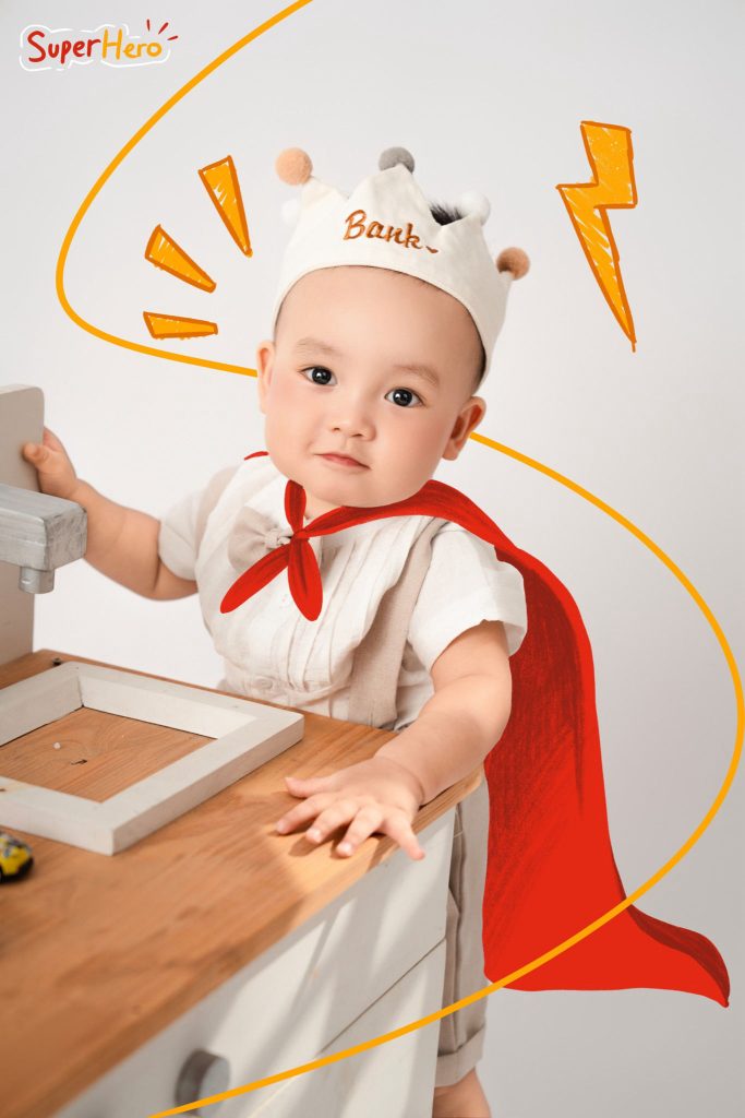Bé đội mũ đầu bếp, đặt tay lên bàn cạnh áo choàng đỏ minh họa