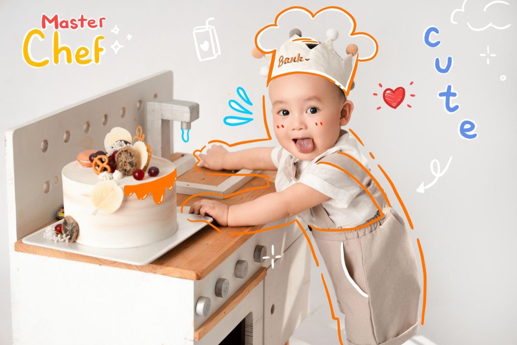 Bé đội mũ đầu bếp ngồi bên bàn có bánh sinh nhật