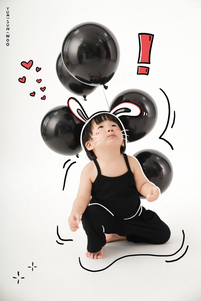 Bé cúi người giữa bóng bay đen, ngước mặt nhìn lên