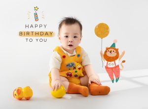 Bé mặc đồ vàng ngồi cùng quả cam trong ảnh thôi nôi