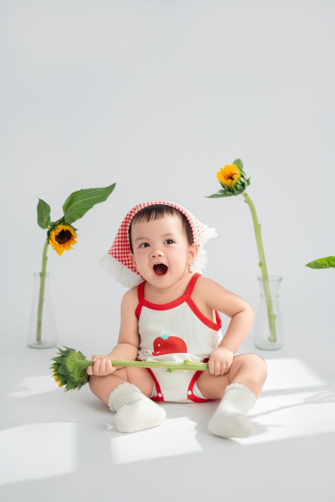 Bé ngồi trên nền sáng cùng chi tiết cây hoa minh họa