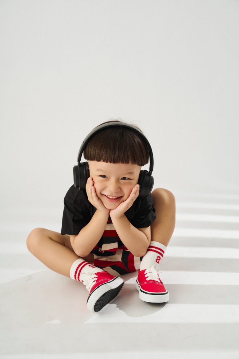 Bé ngồi chống cằm trong trang phục đen đỏ trên nền trắng