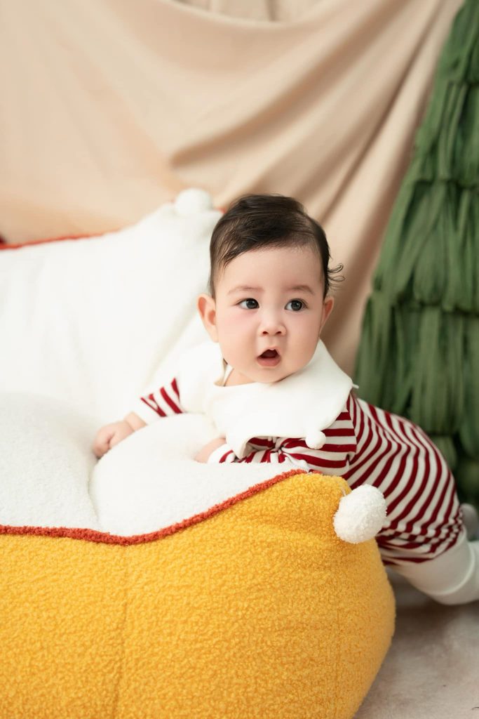 Bé vịn gối đỏ trắng trên chiếc giường màu vàng