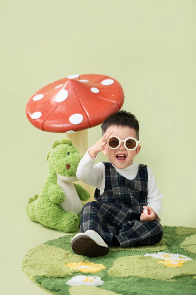 Bé ngồi đeo kính tròn sẫm màu trong bối cảnh rừng