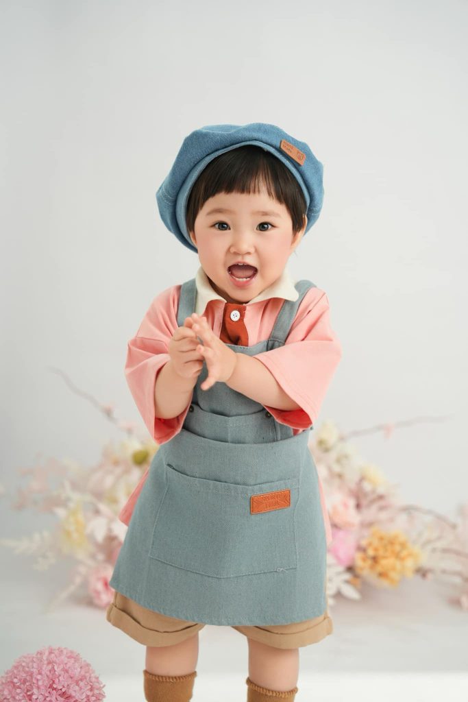 Bé cười vỗ tay trong bộ tạp dề xanh