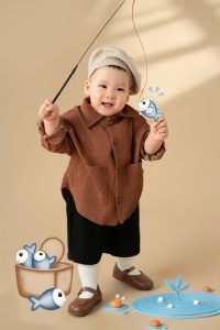 Bé mặc áo nâu tạo dáng trong bối cảnh xe và đồ chơi minh họa