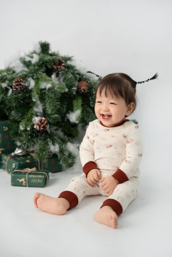 Bé ngồi cạnh cây thông trong bối cảnh Giáng sinh