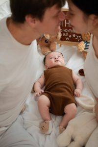 Ba mẹ cùng hôn bé mặc đồ nâu đang nằm trên giường