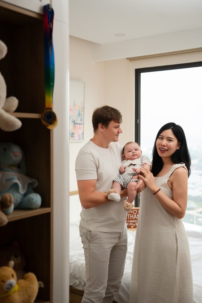 Ba mẹ đứng bế bé trong căn phòng sáng