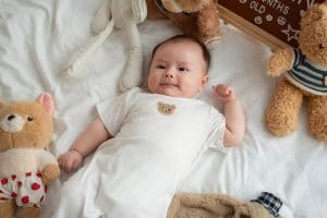 Chụp newborn tại nhà ở Hưng Yên: ekip mang gì tới, giữ phòng ấm và theo nhịp bú, ngủ của bé ra sao? 7 Chân dung bé mặc đồ trắng giơ một tay trên nền giường