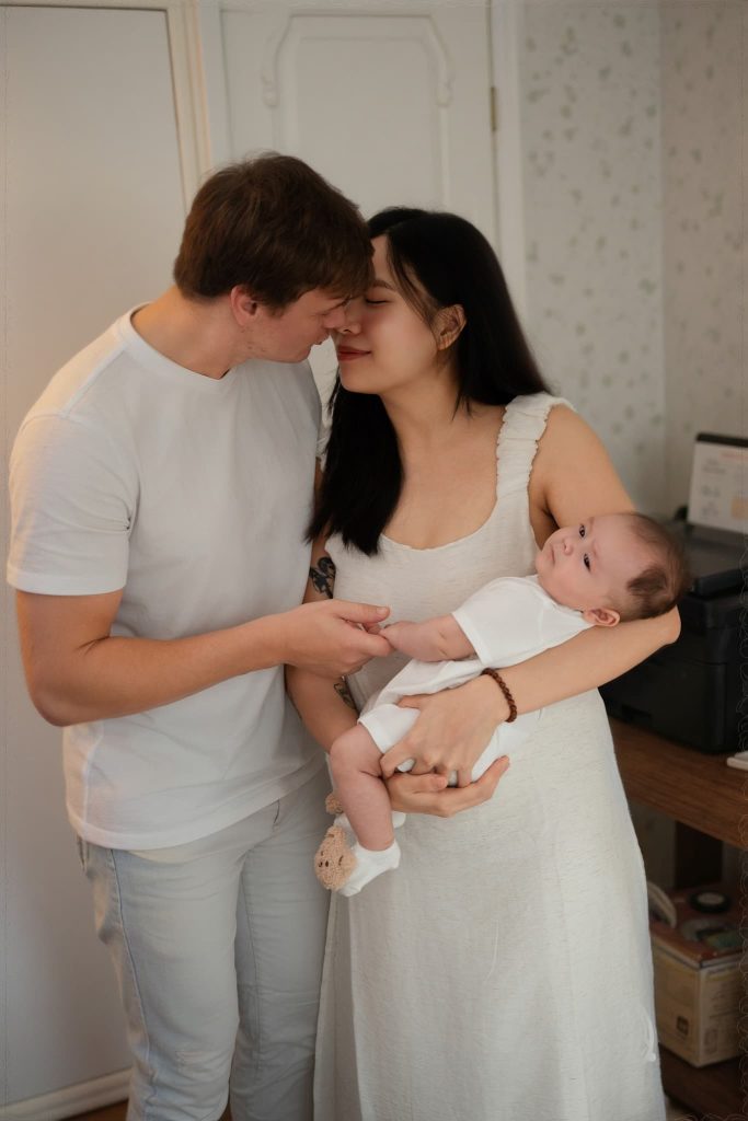 Chụp ảnh sơ sinh tại nhà: chuẩn bị một góc phòng vừa đủ 1 Bố nhìn bé trong vòng tay mẹ bên giường trắng