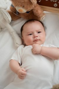 Bé đưa tay chạm má khi nằm trên nền trắng