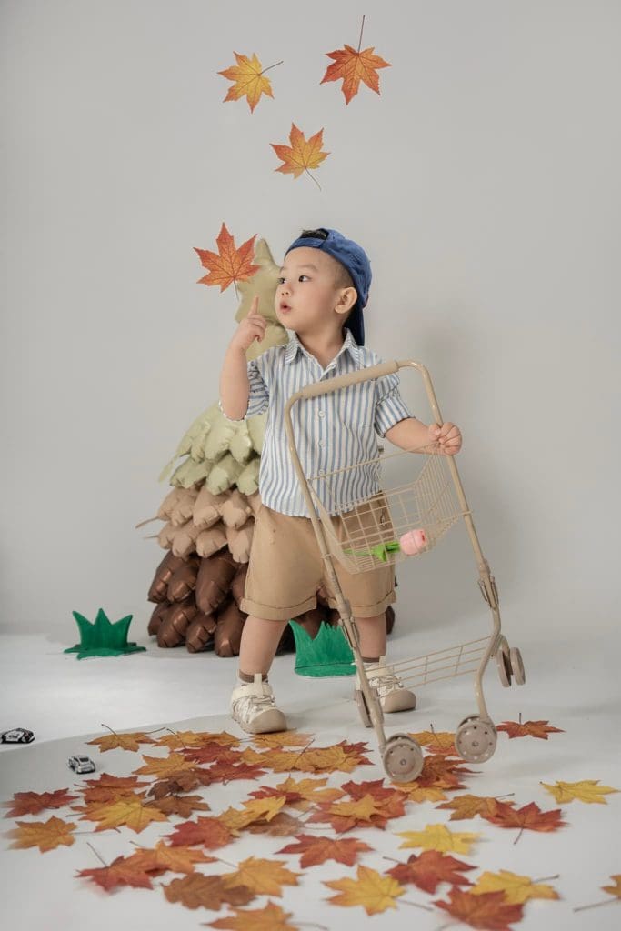 Bé đứng giơ tay đón lá trong bối cảnh rừng trang trí