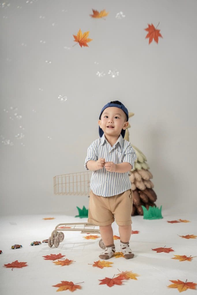 Bé đứng nhìn máy ảnh bên những cây nấm và thú bông