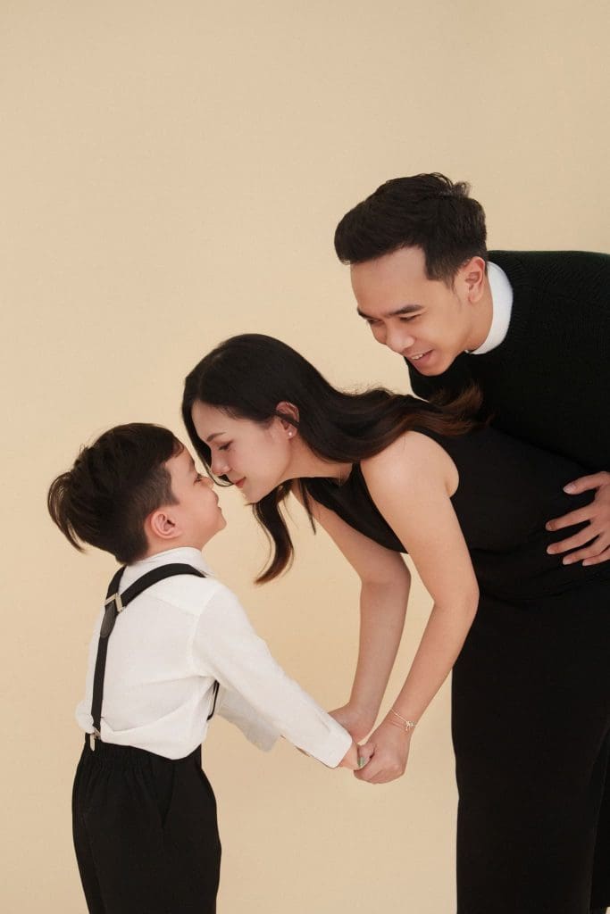 Bố hôn mẹ, bé trai đứng gần trên nền màu be