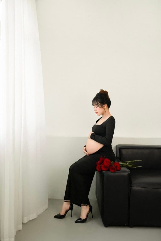 Mẹ bầu mặc váy đen ngồi trên ghế trong không gian sáng