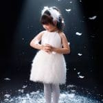 Mẫu nhí mặc váy trắng tạo dáng trong bối cảnh ánh sáng sân khấu