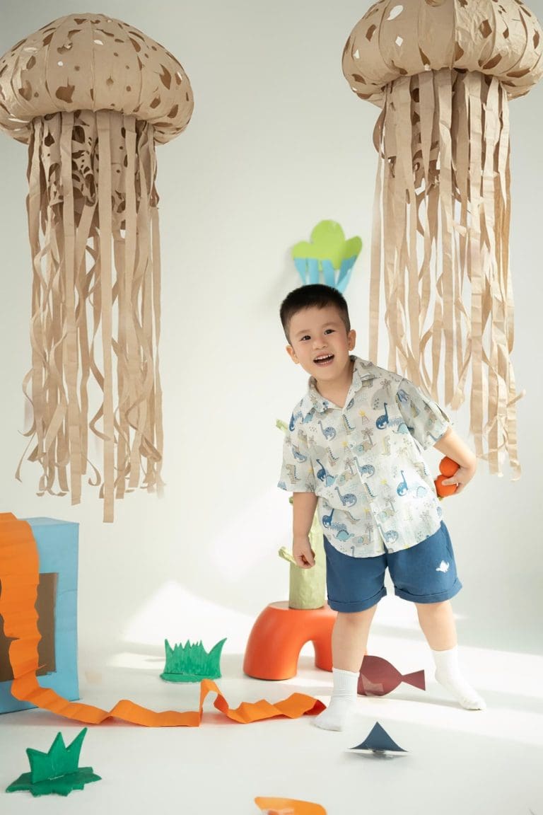 Bé mặc áo hoa đứng trong bối cảnh đồ thủ công và giấy màu