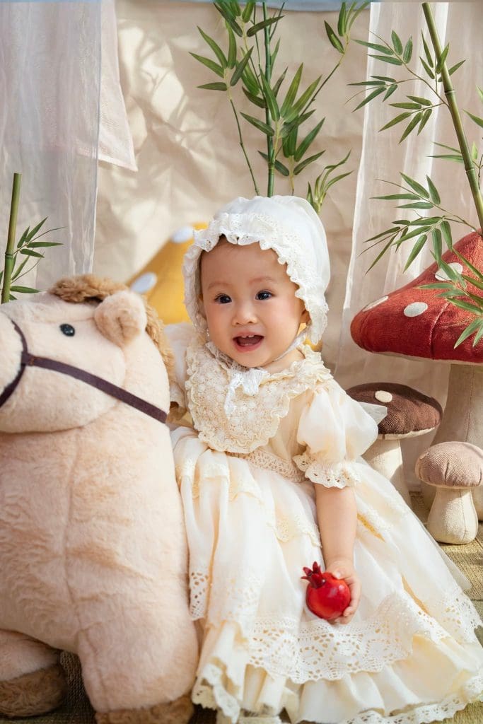 Bé ngồi cạnh ngựa bông và những cây nấm trang trí