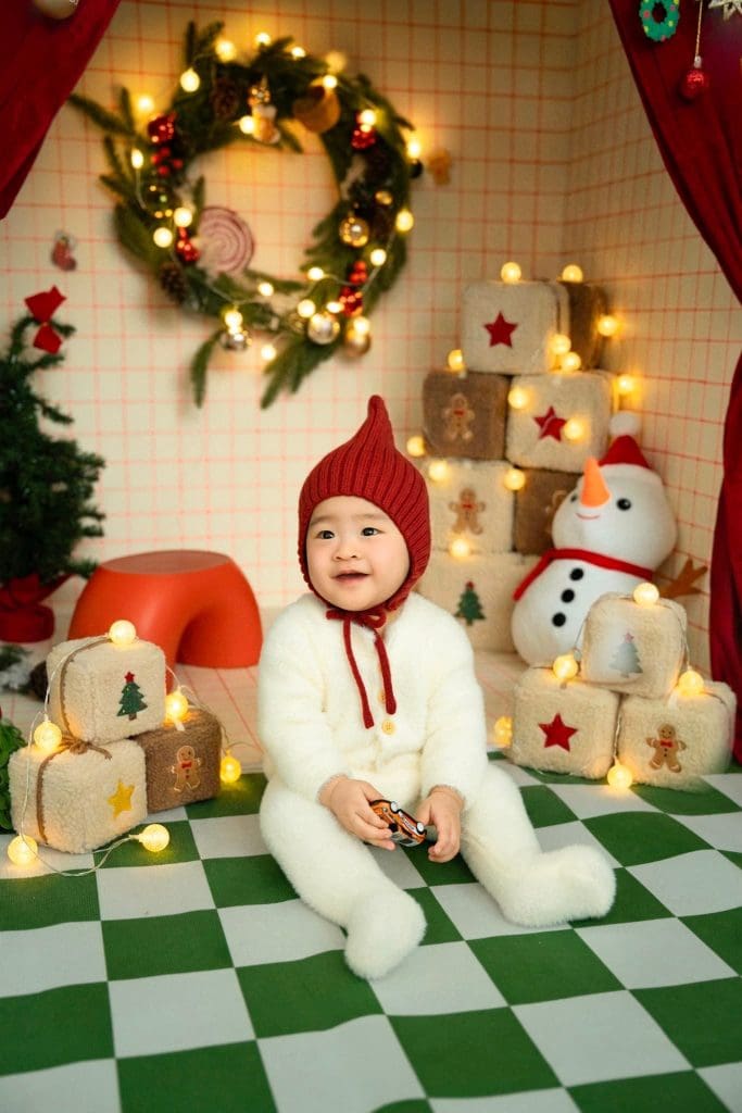 Bé cười giơ hai tay trong bộ đồ trắng và mũ đỏ