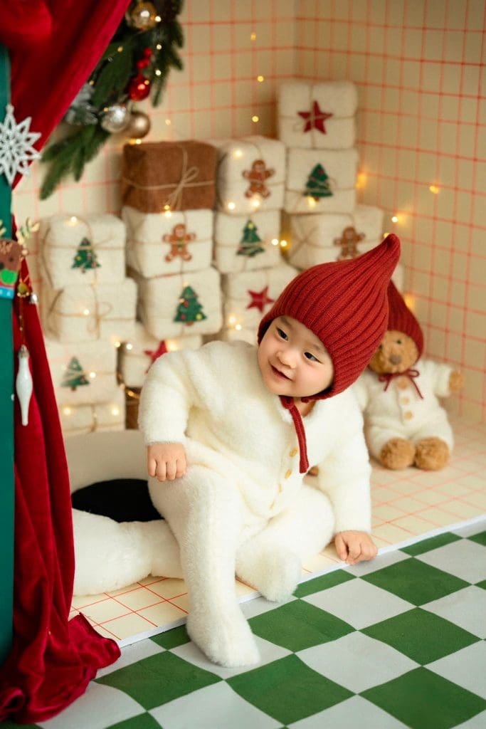 Bé đứng vịn hộp quà trắng trong bối cảnh Giáng sinh