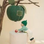 Bé ngồi trên bục trắng, nhìn cành táo bên cạnh