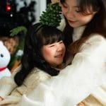 Mẹ ôm bé gái mặc váy đỏ trong bối cảnh Noel